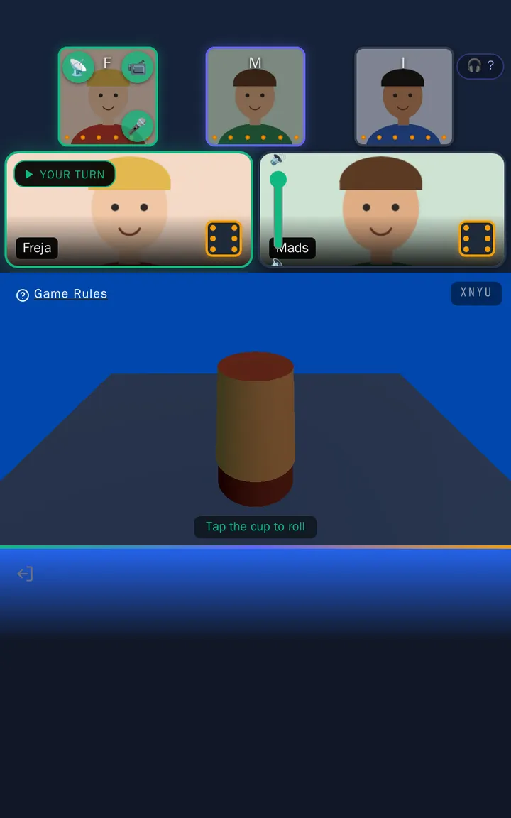 Freja's screen at the start of the round: the players' camera tiles, the cup on the table and the hint "Tap the cup to roll"